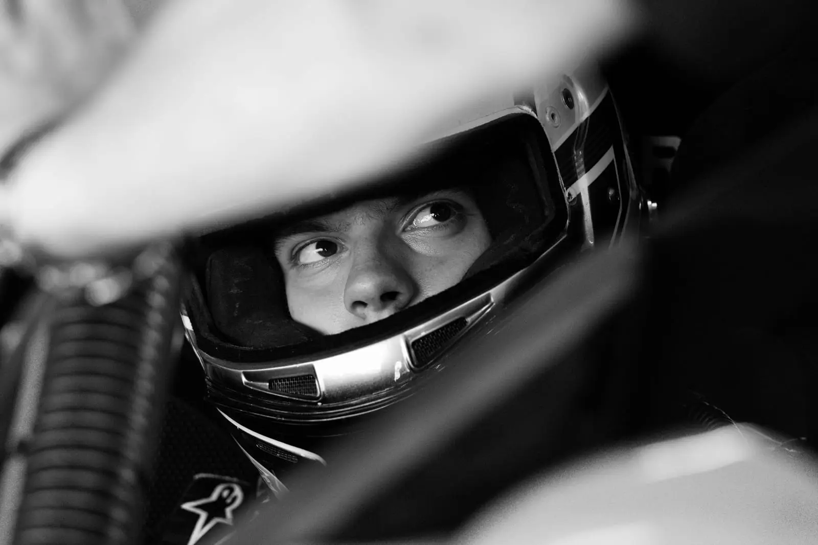 Black-and-white close-up of a driver in a full-face helmet, eyes on the road ahead.