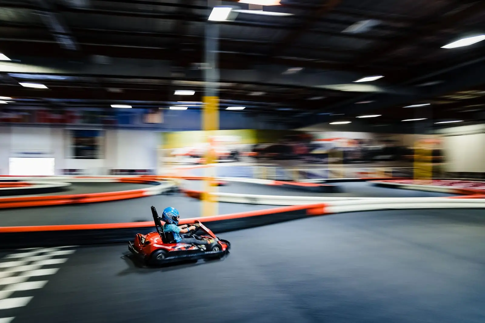 A red go-kart sweeps through an indoor track with motion blur.