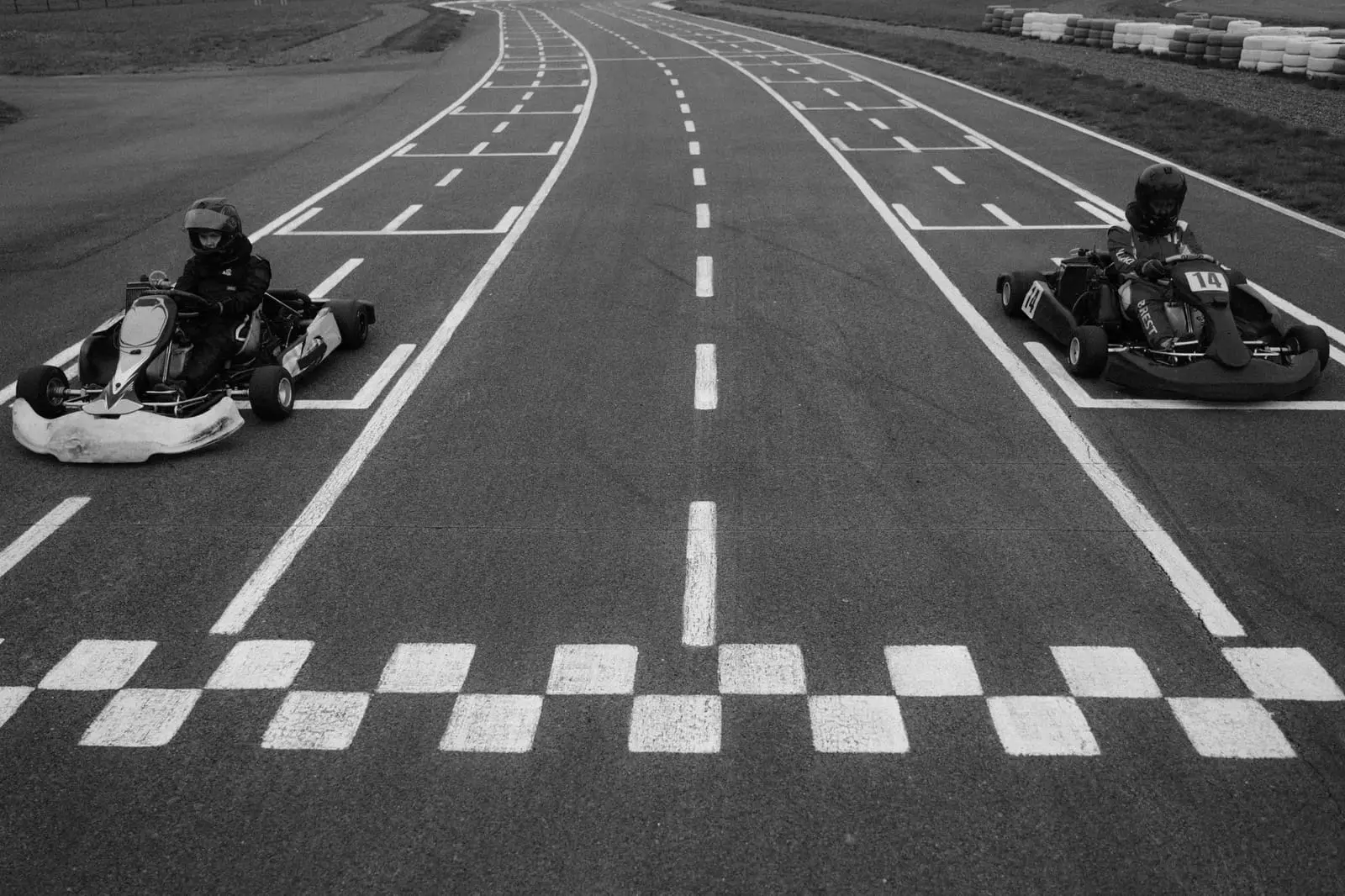 Two go-karts line up behind a chequered start line in black and white.