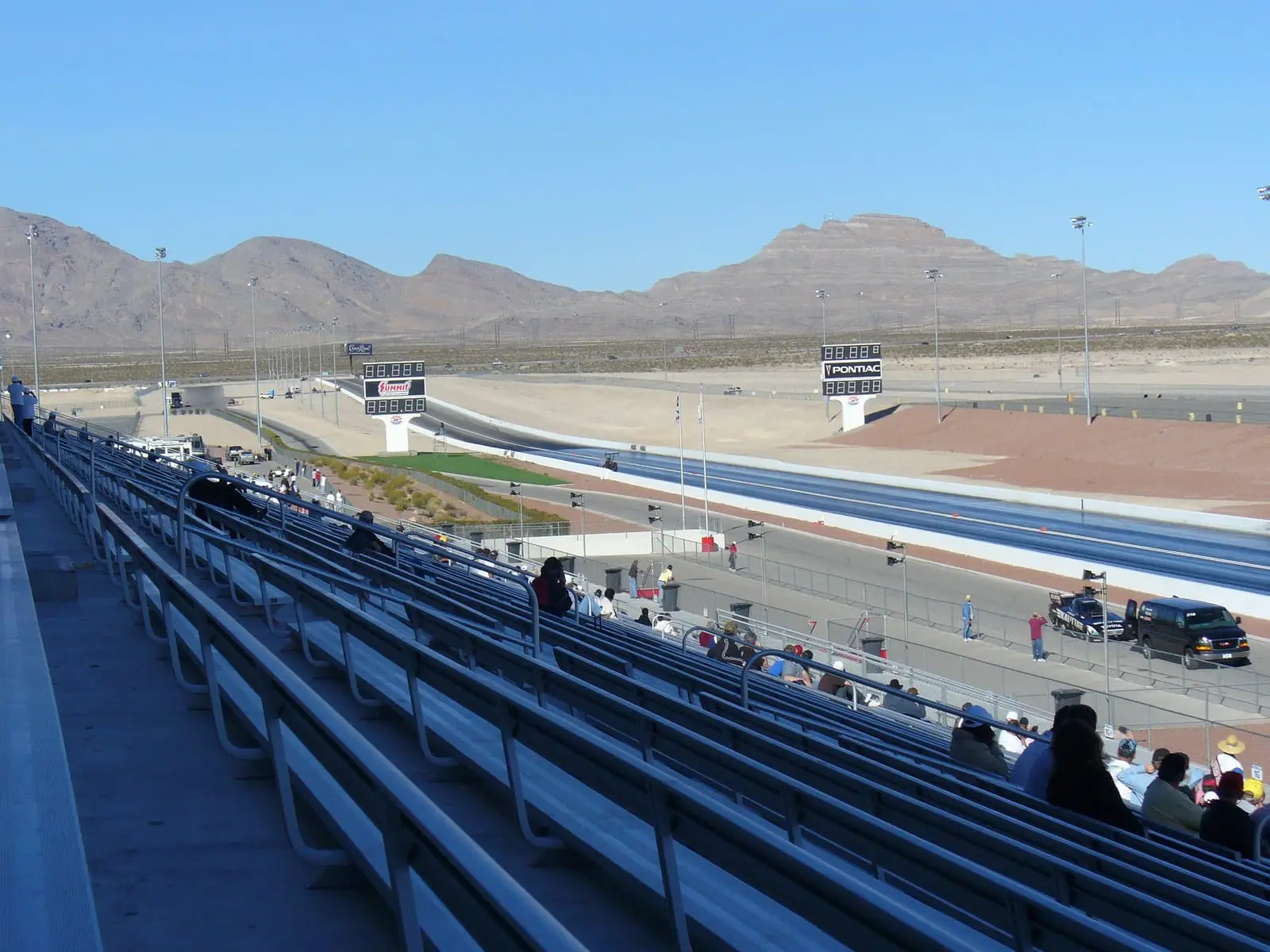 Spectators in the stands beside the drag strip at Las Vegas Motor Speedway, with mountains on the horizon.