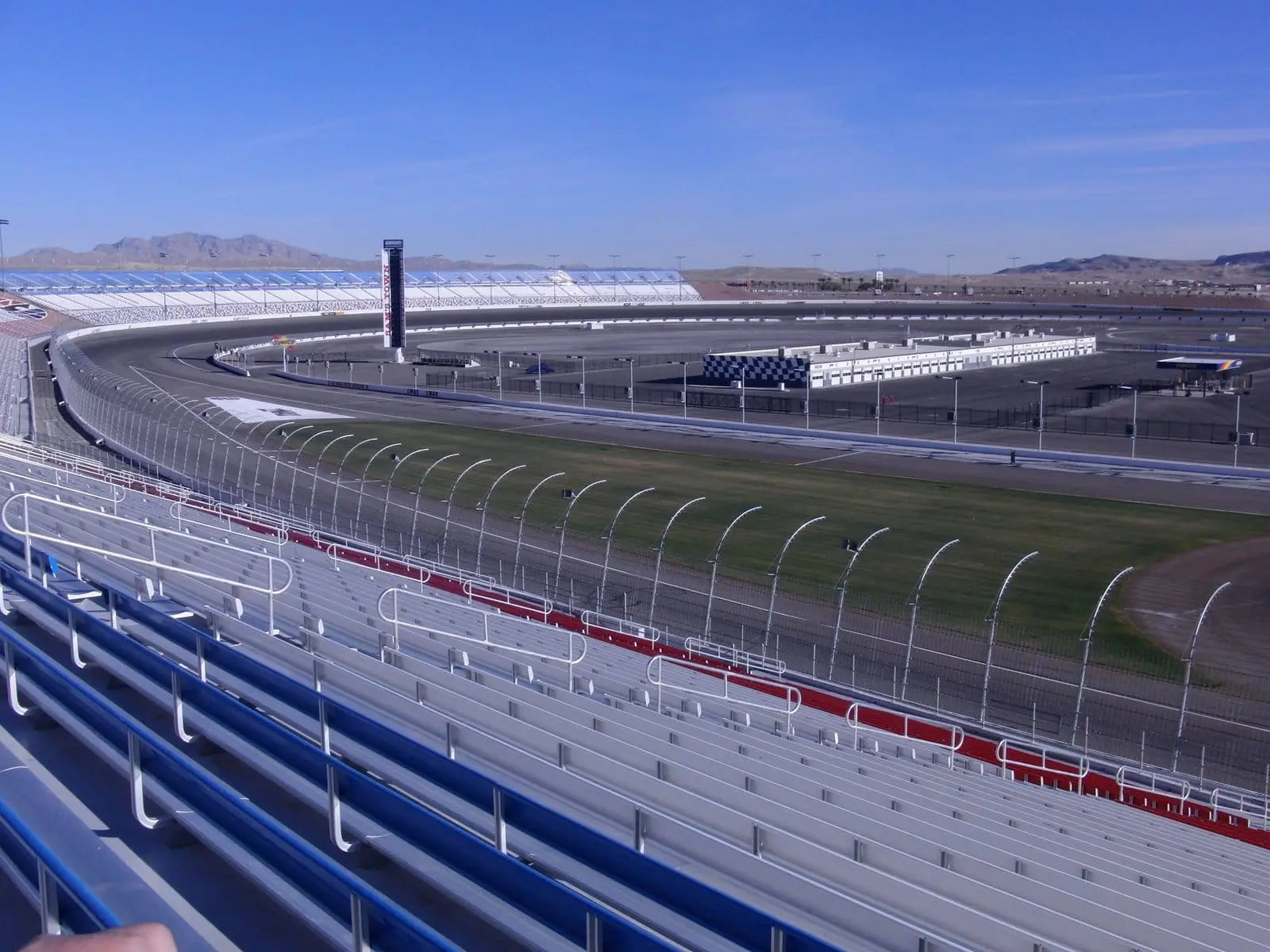 Empty grandstands curving around the oval at Las Vegas Motor Speedway with desert mountains behind.