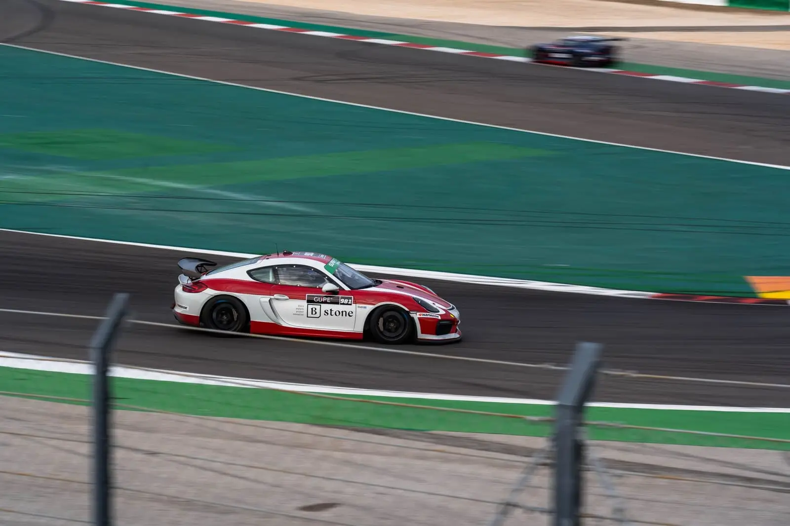 A red and white race car on a wide circuit with green run-off.