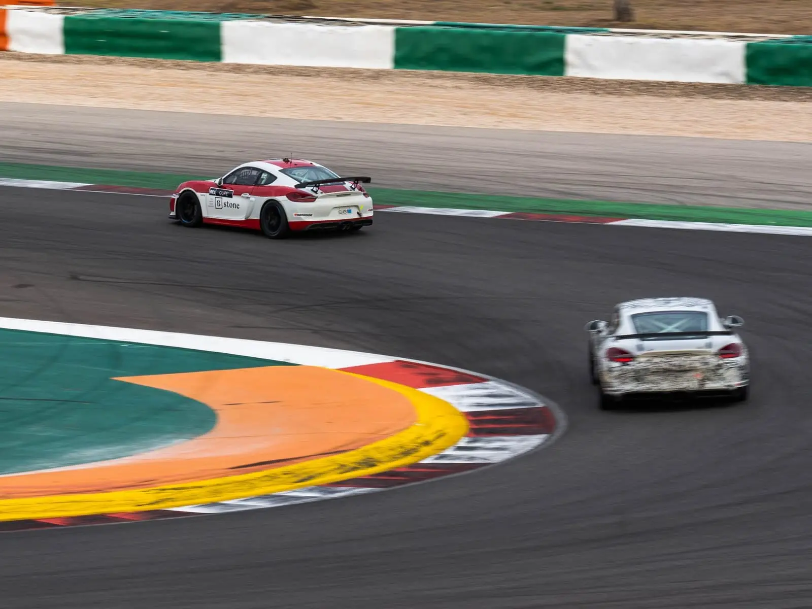Two race cars clip the orange and red kerbs at a corner apex.