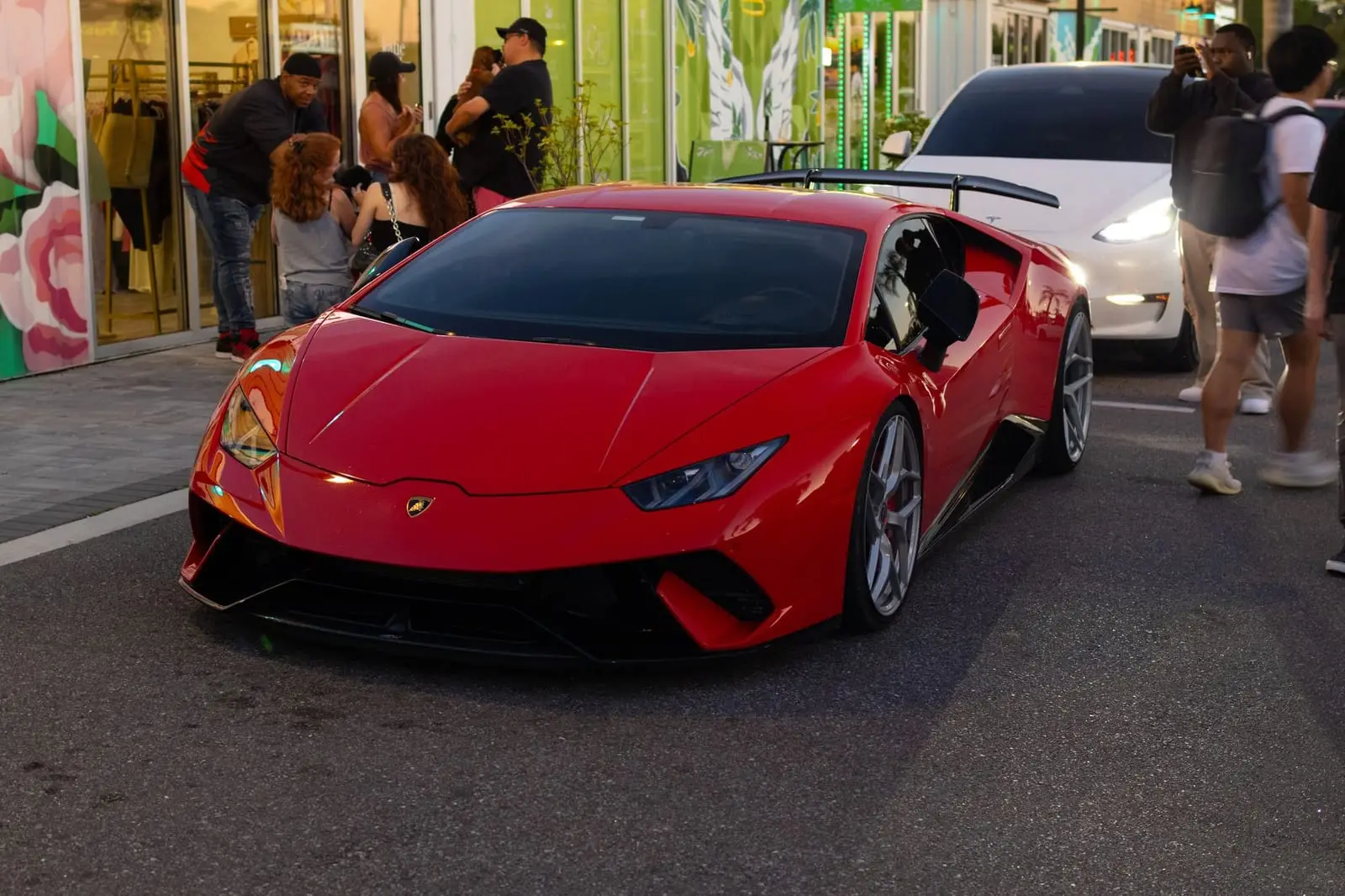 A red supercar parked on a busy street at a car meet.