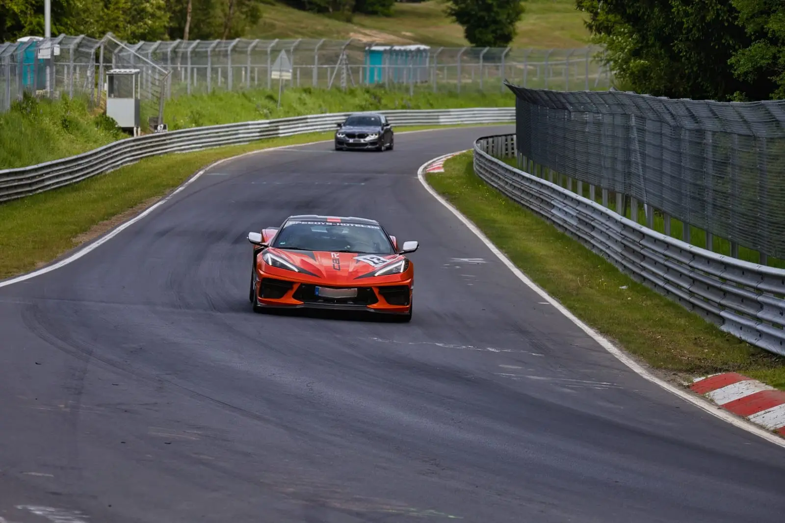 A red sports car leads through a tree-lined corner on a race circuit.